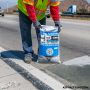 A bag of HP Concrete Cold Patch held by a contractor beside a freshly patch area,'