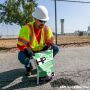 Contractor in safety gear applying HP Asphalt Cold Patch to a pavement crack.'