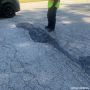 Top Patch Kit used to repair a cracked asphalt driveway, with a contractor in safety gear inspecting the finished patch.
'