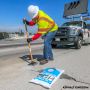 Worker in safety gear compacting HP Concrete Cold Patch on a highway using a hand tamper.'