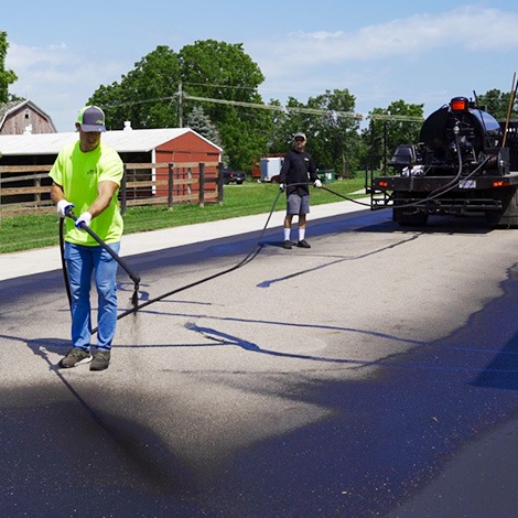 Crew applying asphalt sealer with spray system on driveway