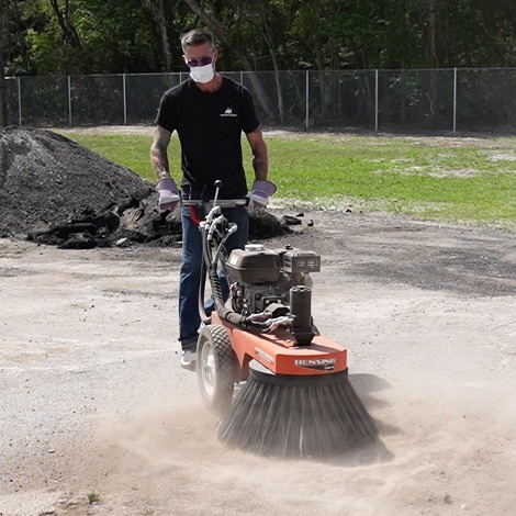Man using power broom for asphalt surface prep before sealcoating